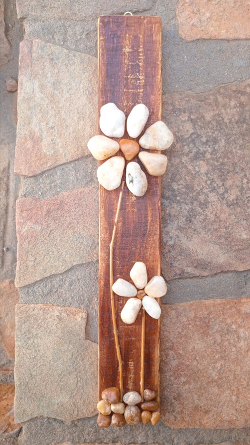 Handcrafted pebble flower wall art made with natural river stones and twigs on a whitewashed wooden base, inspired by the Kuiseb River landscape in Namibia.
